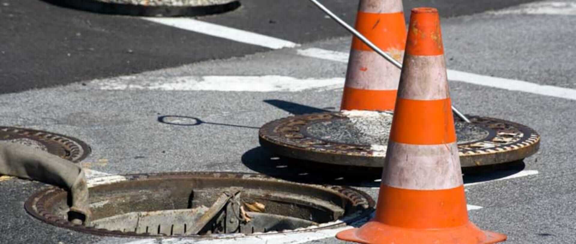 En åben kloakdæksel, ved siden af står to pyloner