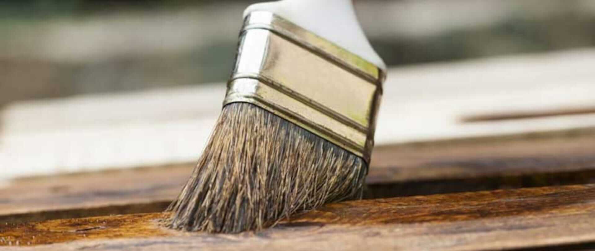 En pensel påfører træolie på et stykke træ.