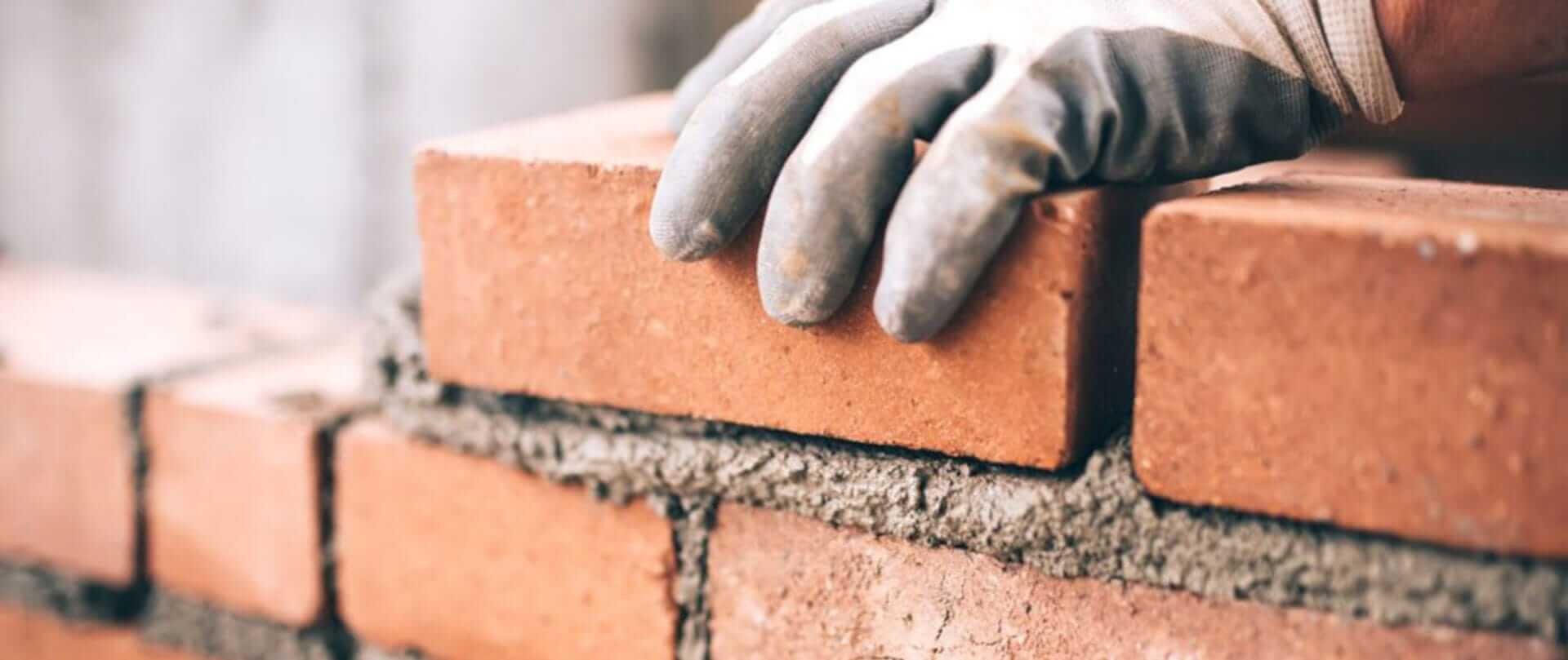 En hånd placerer en mursten på en mur.