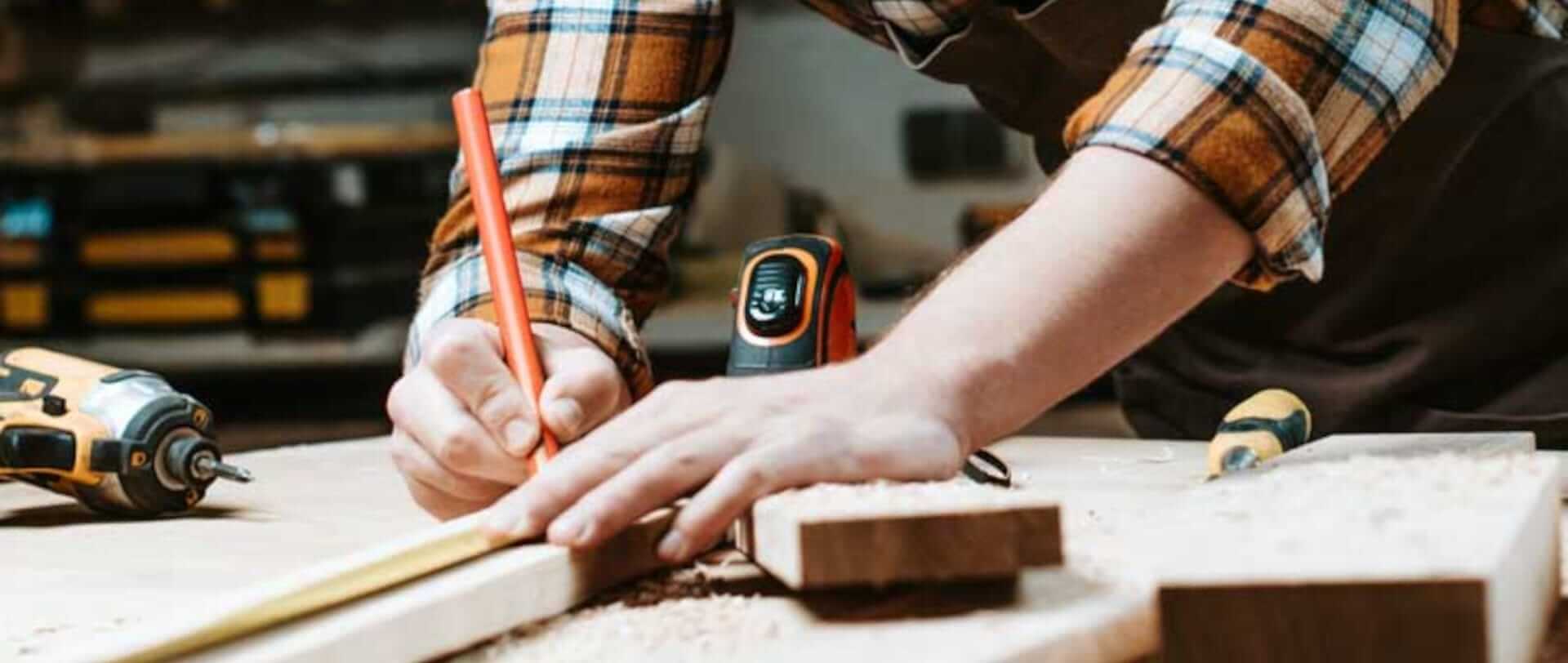 Mand tegner noget med blyant på træ, han bærer en ternet skjorte.