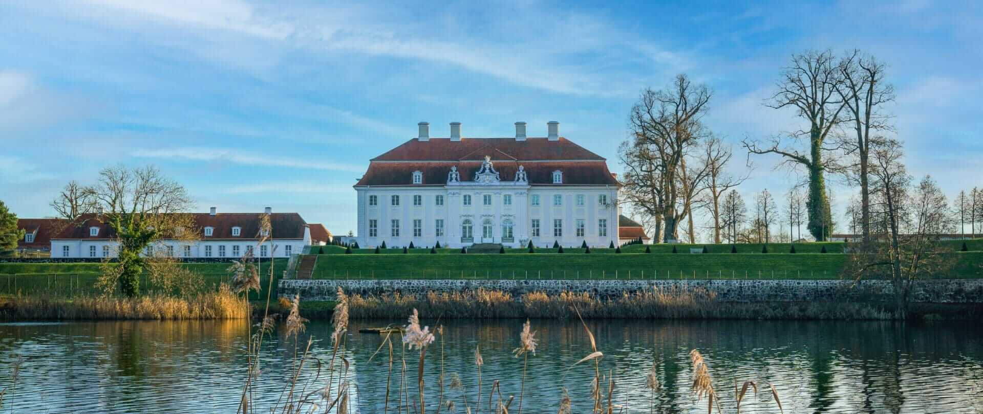 En ejendom på en grøn eng med en sø i forgrunden